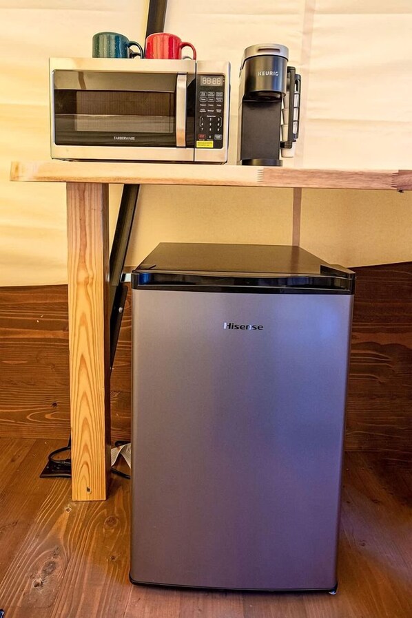 A compact refrigerator with a Hisense logo, a microwave, and a Keurig coffee maker on a wooden table.