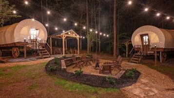 Dos tiendas de campaña cubiertas con estructuras de madera, un hoyo para la hoguera y asientos al aire libre.