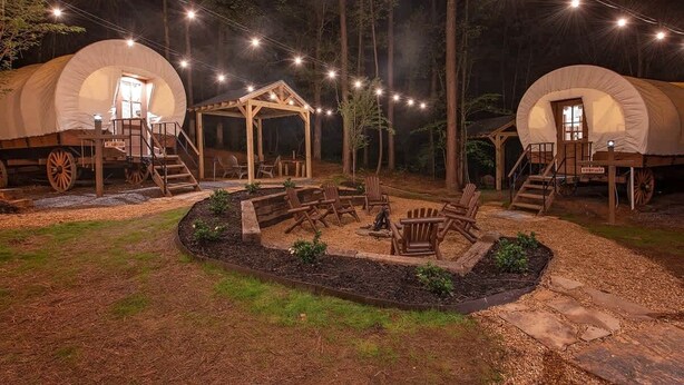 Two covered tents with wooden structures, a fire pit, and outdoor seating.