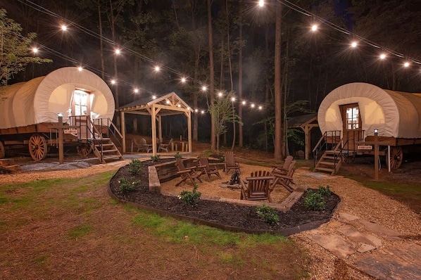 Dos tiendas de campaña cubiertas con estructuras de madera, un hoyo para la hoguera y asientos al aire libre.