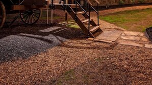 A rustic wooden cabin with a covered wagon attached, a staircase leading to the wagon, and a stone wall with windows.