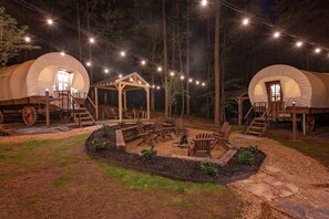 Two covered tents with wooden structures, a fire pit, and outdoor seating. - Beautiful Glamping Wagon Great for Outdoor Adventures in Tennessee (Benton)