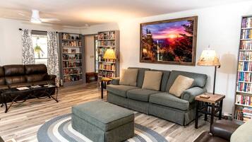 Un salon comprenant un canapé, un pouf, une table basse et des étagères remplies de livres.