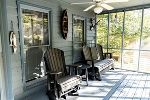 A covered porch with two Adirondack chairs, a small table, and a ceiling fan.