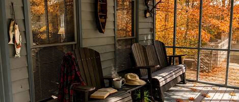A porch with two Adirondack chairs, a bench, and a ceiling fan.