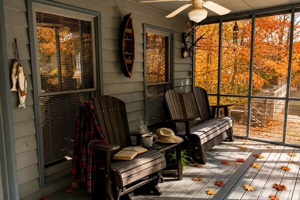 A porch with two Adirondack chairs, a bench, and a ceiling fan.