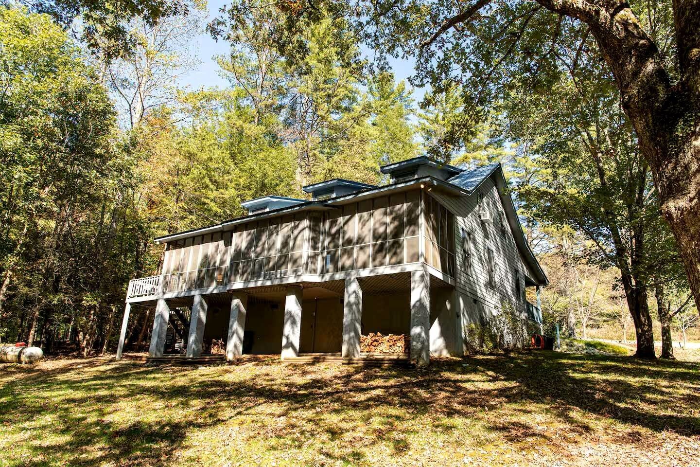 Une cabane rustique dotée d’un porche, entourée d’arbres.