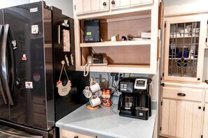Una cocina compacta con un refrigerador negro, una cafetera y un mueble pequeño con puerta de vidrio.