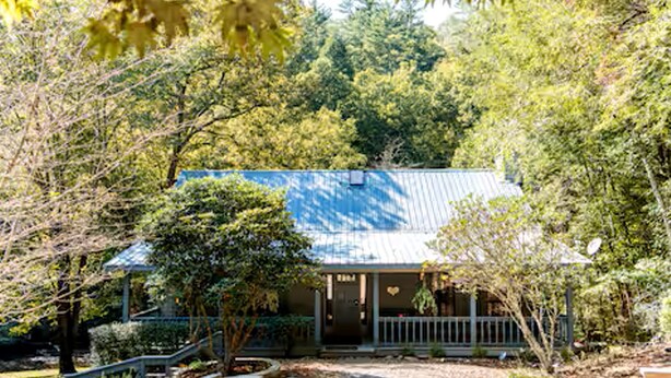 A house with a blue roof, surrounded by trees and a gravel pathway.