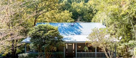 A house with a blue roof, surrounded by trees and a gravel pathway.