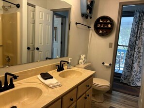 A bathroom with two sinks, a toilet, a mirror, a towel rack, and a window with a view.