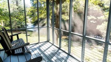 A covered outdoor area with a wooden deck, a bench, and a view of a natural landscape.