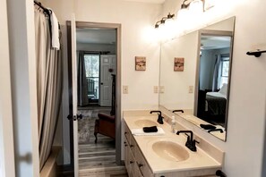 Une salle de bain avec deux lavabos, un grand miroir et une porte donnant sur un couloir.