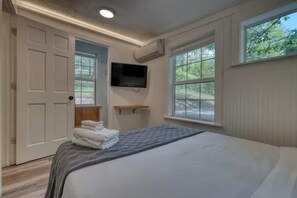 Ein Schlafzimmer mit Bett, Fernseher, Tür und Fenstern.