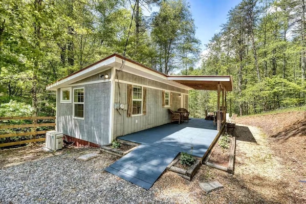 A cabin with a covered porch, a gravel driveway, and a forested backdrop.
