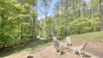 A forested area with a gravel path, two white chairs, and a small fire pit.