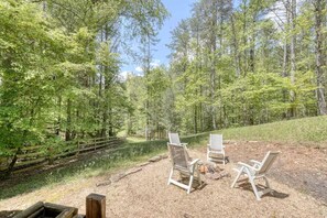 A forested area with a gravel path, two white chairs, and a small fire pit. - Cozy Cabin with Direct Access to the Toccoa River, a Perfect Escape for Fishing Lovers in Suches, Georgia (Suches)