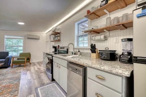 A modern kitchen with granite countertops, a built-in oven, and a dishwasher. There are wooden shelves above the counter and a window providing natural light. - Cozy Cabin with Direct Access to the Toccoa River, a Perfect Escape for Fishing Lovers in Suches, Georgia (Suches)