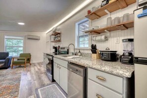 Eine moderne Küche mit Granit Arbeitsplatten, einem eingebauten Backofen und einem Geschirrspüler. Darüber befinden sich Holzregale und ein Fenster lässt natürliches Licht herein.