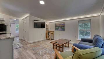A spacious living area with a kitchen, a dining table, a sofa, and a TV mounted on the wall.