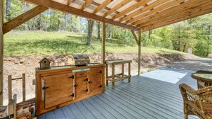 A wooden deck with a grill, a table, and wicker chairs. - Cozy Cabin with Direct Access to the Toccoa River, a Perfect Escape for Fishing Lovers in Suches, Georgia (Suches)