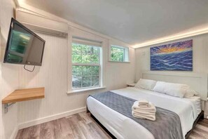 Une chambre à coucher avec un lit, un téléviseur fixé au mur, une fenêtre et un tableau.