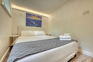 Una camera d'hotel con un letto, un quadro, un comodino e una lampada a parete.