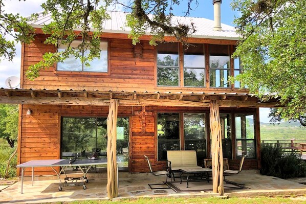 A wooden cabin with a covered patio, large windows, and a satellite dish.