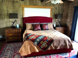 A bed with a red headboard, a patterned blanket, and a wooden floor.