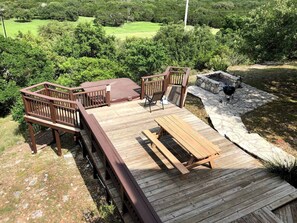 Una terraza de madera con un hogar a piedra, asientos al aire libre y vistas a un paisaje verde.
