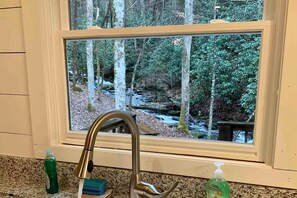 Ein Badezimmer mit Blick auf eine bewaldete Landschaft und einen Bach.