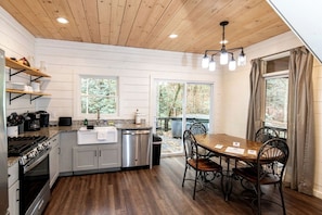 A kitchen with a stove, sink, and dining table with chairs. - Secluded Cabin on Suches Creek and in the National Forest for a Relaxing Georgia Getaway (Suches)