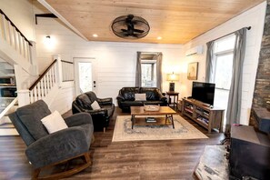 Un salon avec un escalier, une cheminée, un téléviseur et un coin repas.