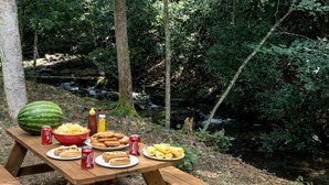 Una mesa de picnic con comida y bebidas en un área boscosa.