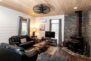 Una sala de estar acogedora con un sofá de cuero, un televisor, una chimenea y una pared de piedra.