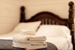Una cama bien hecha con cabecera de madera, sábanas blancas y una pila de toallas dobladas.