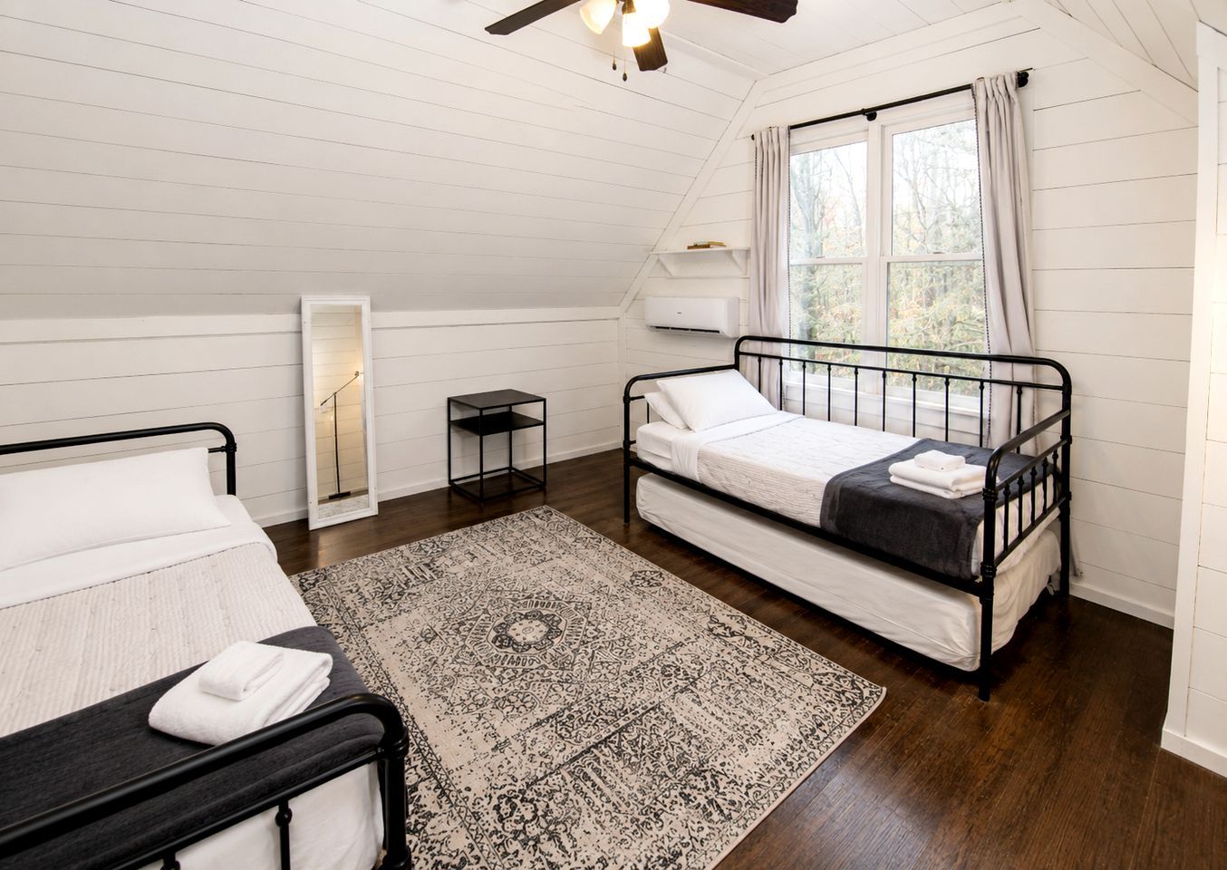 A bedroom with a bed, a bedside table, a floor lamp, a window with curtains, and a ceiling fan.