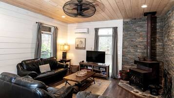 A cozy living room with a leather sofa, a TV, a fireplace, and a stone wall.