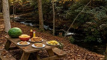 A picnic table set up in a forest with a stream in the background.