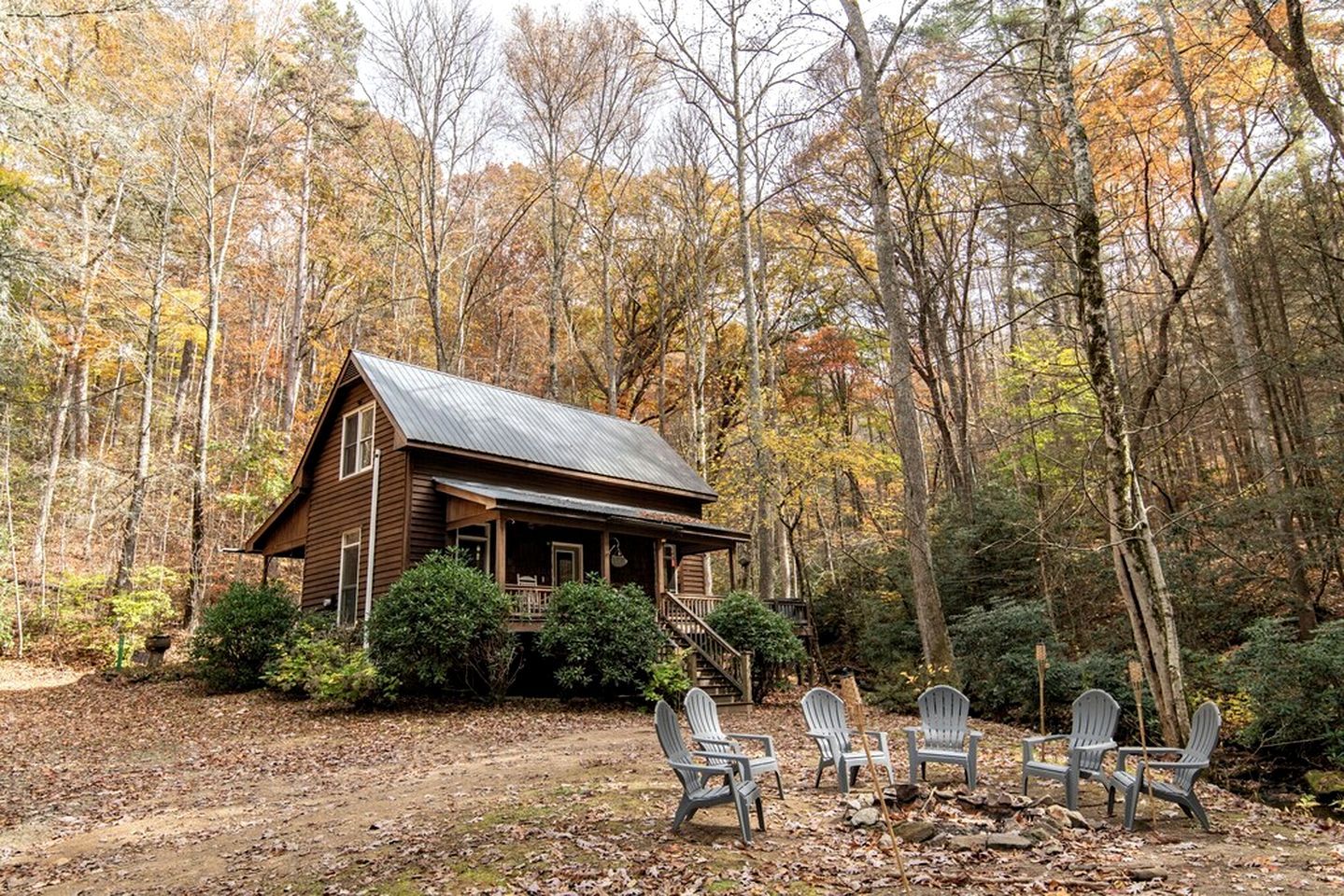 A cabin with a porch, surrounded by trees and a dirt path.