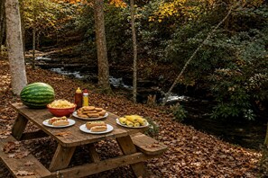 Una mesa de picnic montada en un bosque con un arroyo al fondo.