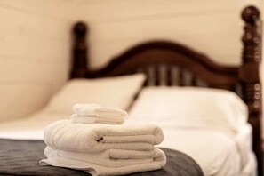 Ein ordentlich bezogenes Bett mit Holz Kopfteil, weißen Bettwäsche und einem Stapel gefalteter Handtücher.