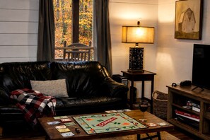 Ein Wohnzimmer mit einer Ledersofa, einem Gesellschaftsspiel, einer Lampe, einem Fernseher und einem Bücherregal.