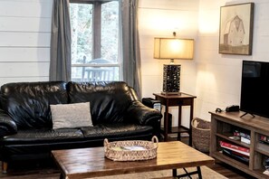 A living room with a black leather sofa, a wooden coffee table, a lamp, a TV, and a bookshelf.