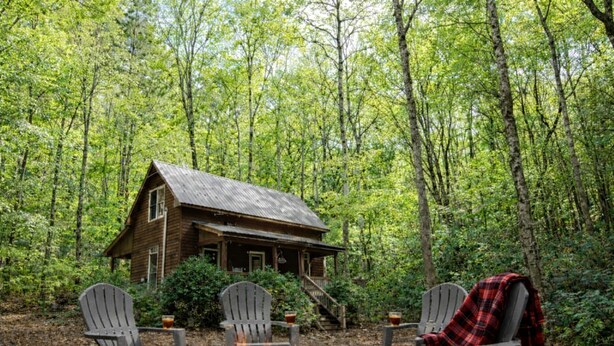 Una cabaña rodeada de bosque, con un brasero y dos sillas Adirondack.