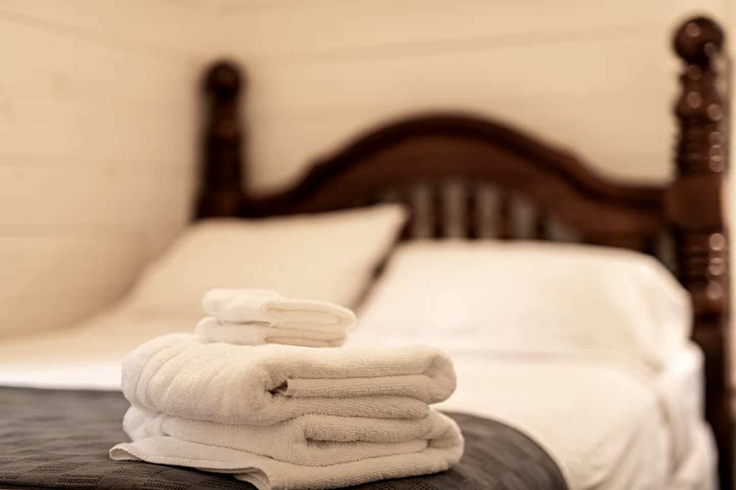A neatly made bed with a wooden headboard, white linens, and a stack of folded towels.