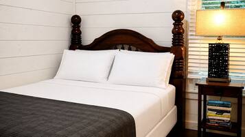 A bed with white bedding, a wooden headboard, and a bedside table with a lamp and books.