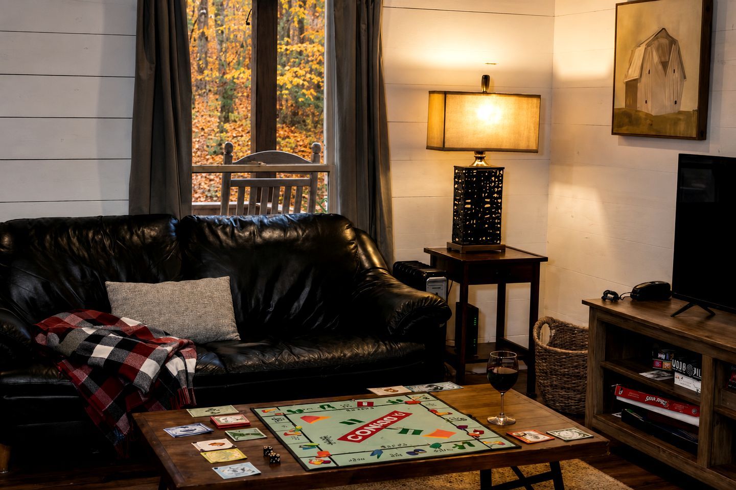 Una sala de estar con un sofá de cuero, un juego de mesa, una lámpara, un televisor y una estantería.