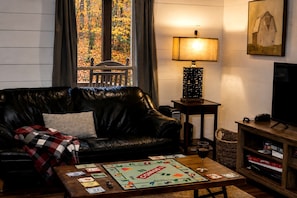 Een woonkamer met een leren bank, een spel, een lamp, een televisie en een boekenkast.