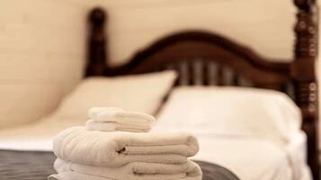 A neatly made bed with a wooden headboard, white linens, and a stack of folded towels.